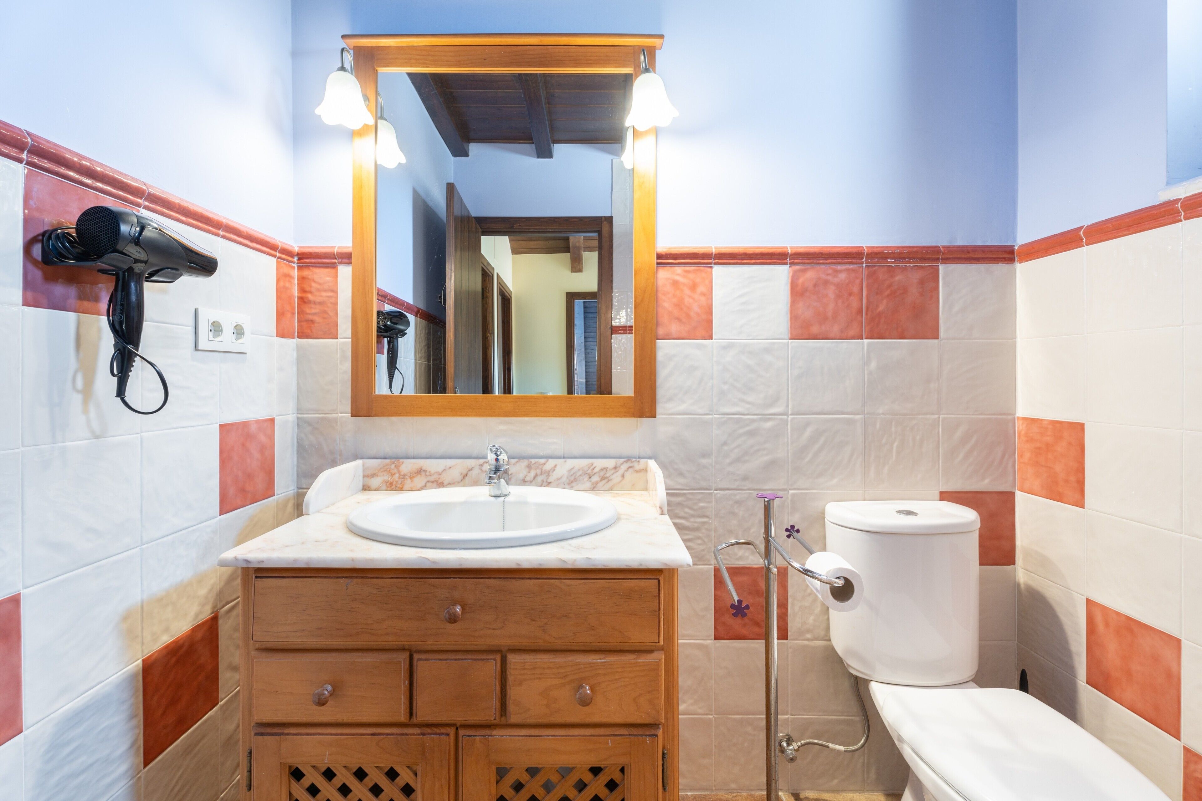 Een badkamer met een wastafel, spiegel, wastafelmeubel, toilet en een aan de muur bevestigde haardroger.