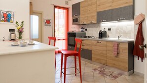 Een moderne keuken met houten kastjes, een centraal eiland, rode stoelen en een rode hanglamp.