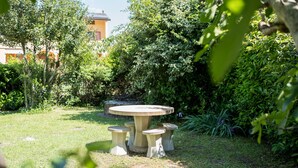 Een tuin met een ronde stenen tafel en vier bijpassende krukjes.