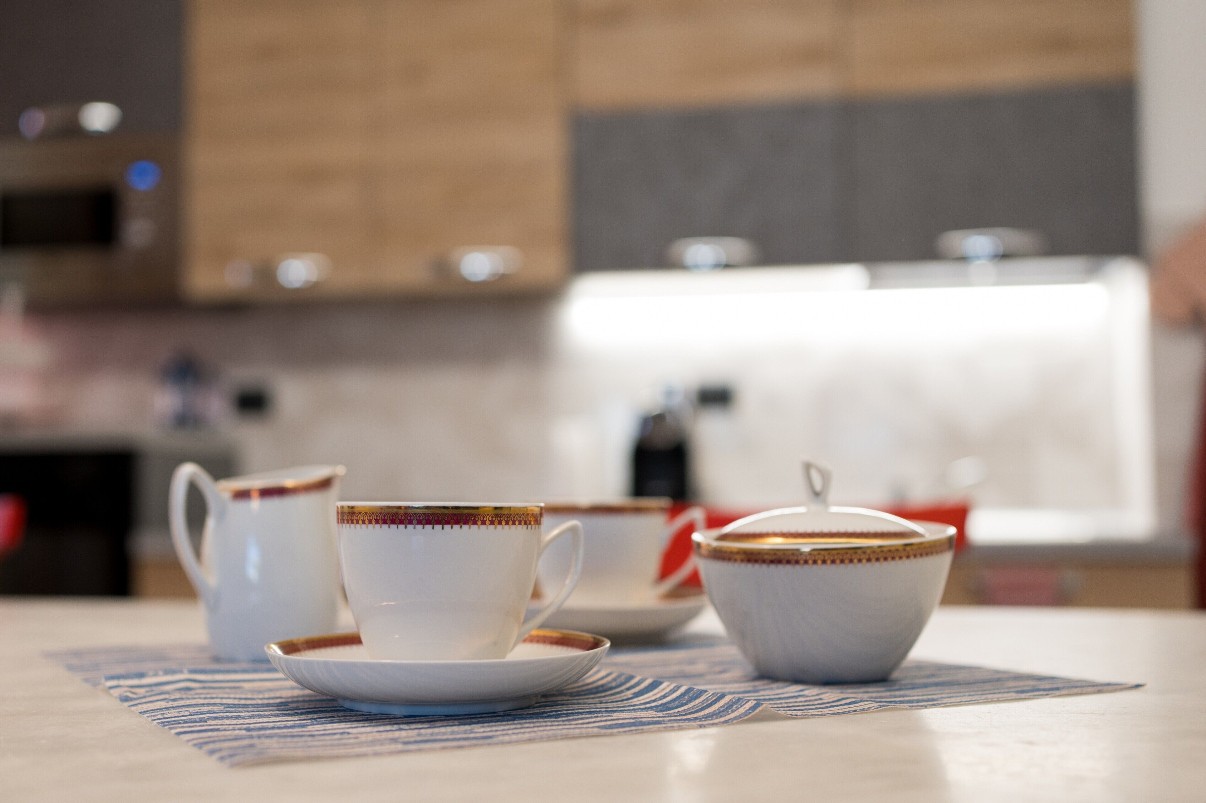 A kitchen with a table set with white cups and saucers, a bowl, and a teapot.