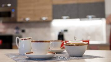 A kitchen with a table set with white cups and saucers, a bowl, and a teapot.