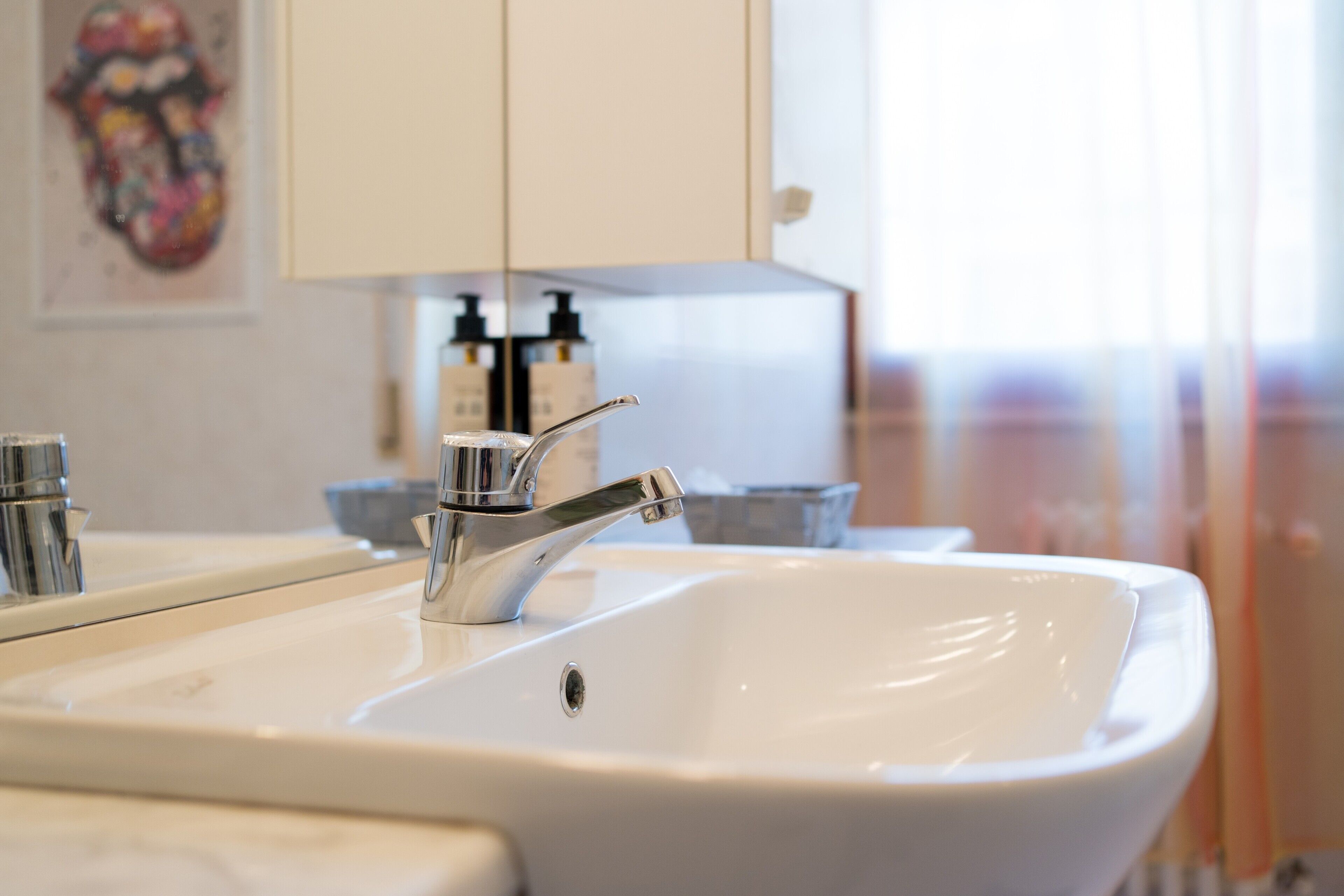 A bathroom sink with a chrome faucet, a mirror, and a white cabinet in the background.