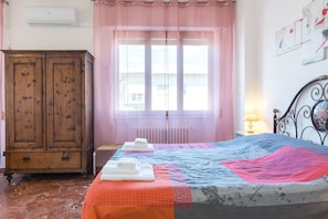 Quarto com cama, guarda-roupa de madeira, janela com cortinas e radiador.