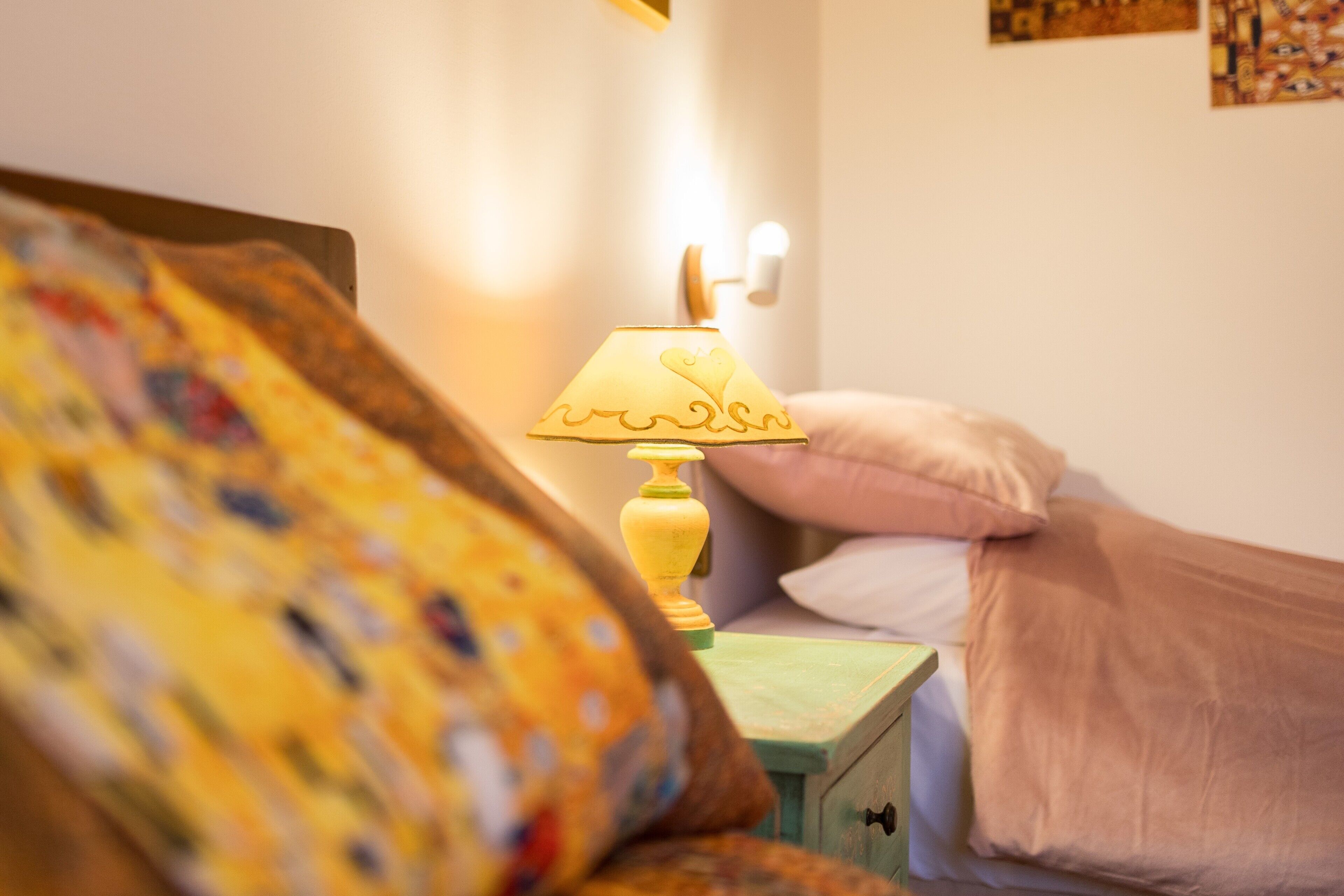 Uma cama com travesseiro, uma mesa de cabeceira com abajur e uma parede com obras de arte.