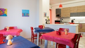 A dining area with tables covered in red and blue tablecloths, wooden chairs, and a central island with a coffee machine. - 'Art Rooms - Banksy Klimt' Rooms with Shared Terrace, Wi-Fi and Air Conditioning (Arezzo)