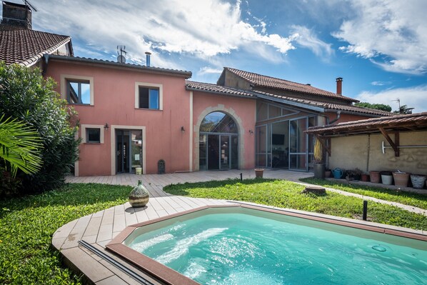 Ein zweistöckiges Haus mit Swimmingpool, überdachter Terrasse und Garten.