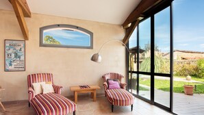 A room with two striped armchairs, a wooden table, a large window, and a poster on the wall. - Spacious House in Marciac with Private Pool and Terrace (Marciac)