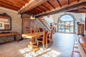 A dining area with a wooden table and chairs, a bench, a staircase, and a view through a large arched window. - Spacious House in Marciac with Private Pool and Terrace (Marciac)