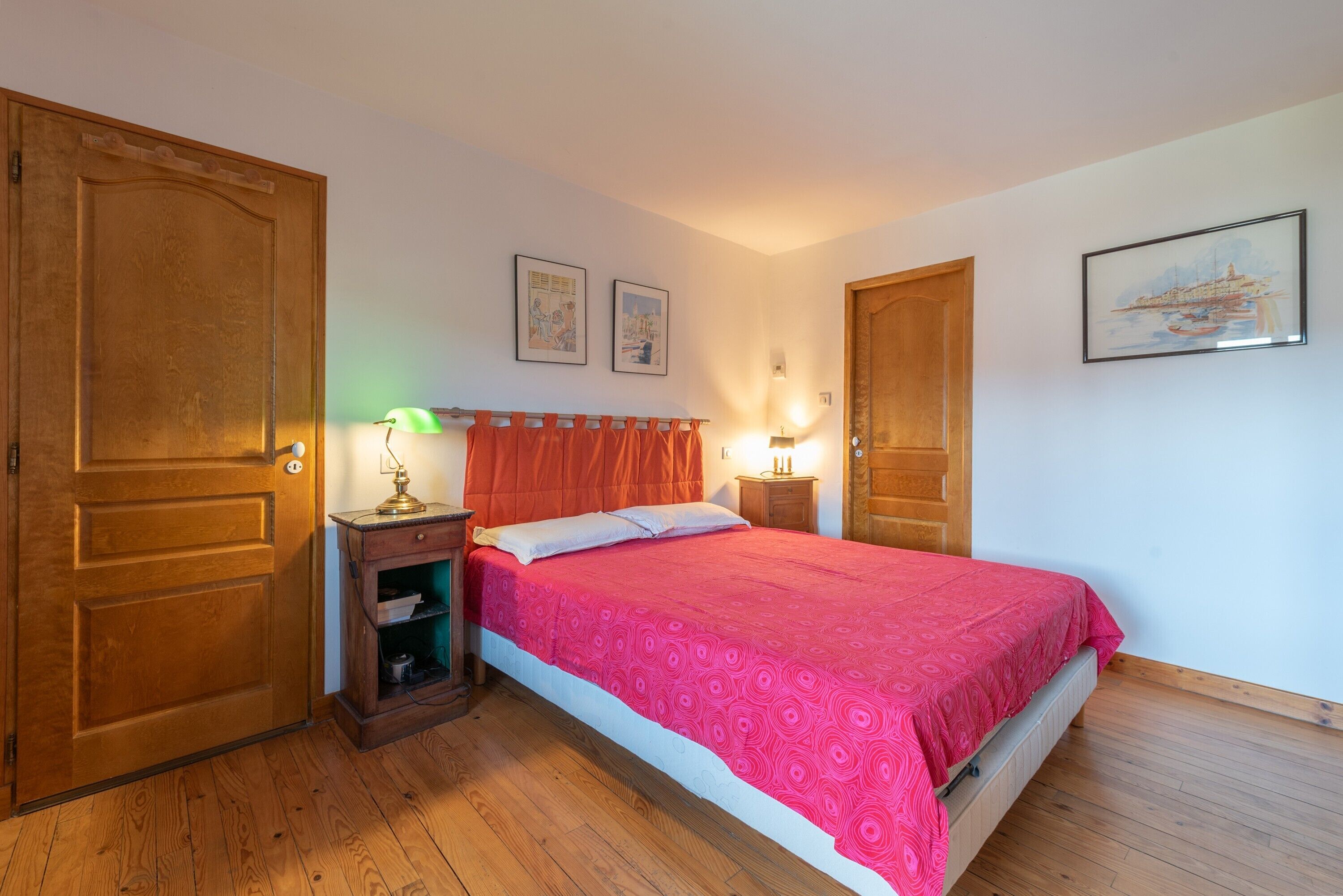 Une chambre à coucher comprenant un lit, une armoire en bois, une table de chevet, une lampe et un tableau encadré accroché au mur.