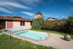 Ein Schwimmbecken mit Glasabdeckung, umgeben von einer Holzterrasse und einer Rasenfläche.