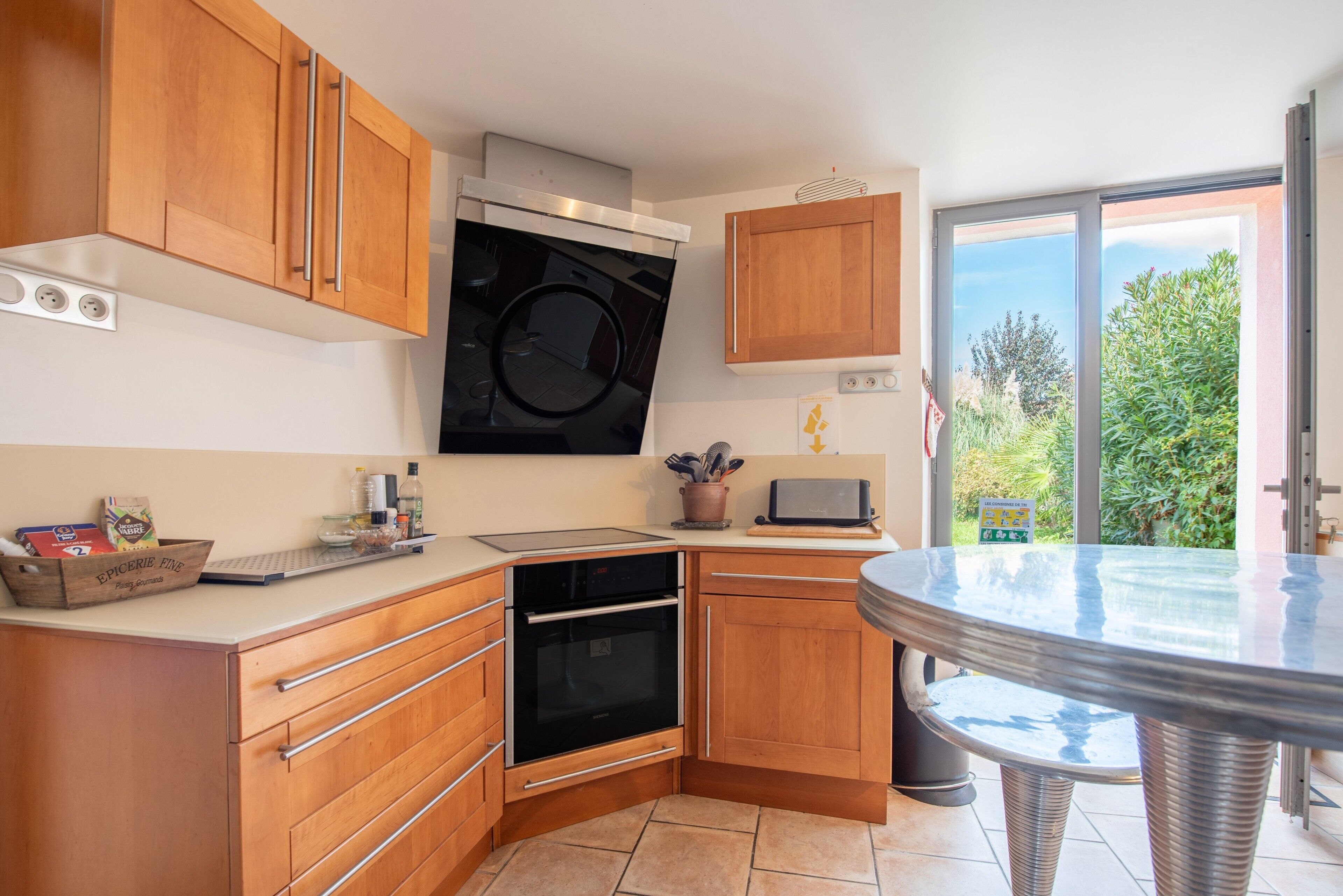 A kitchen with wooden cabinets, a built-in oven, a microwave, and a large window offering a view of greenery.