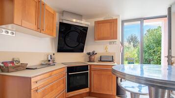 A kitchen with wooden cabinets, a built-in oven, a microwave, and a large window offering a view of greenery.