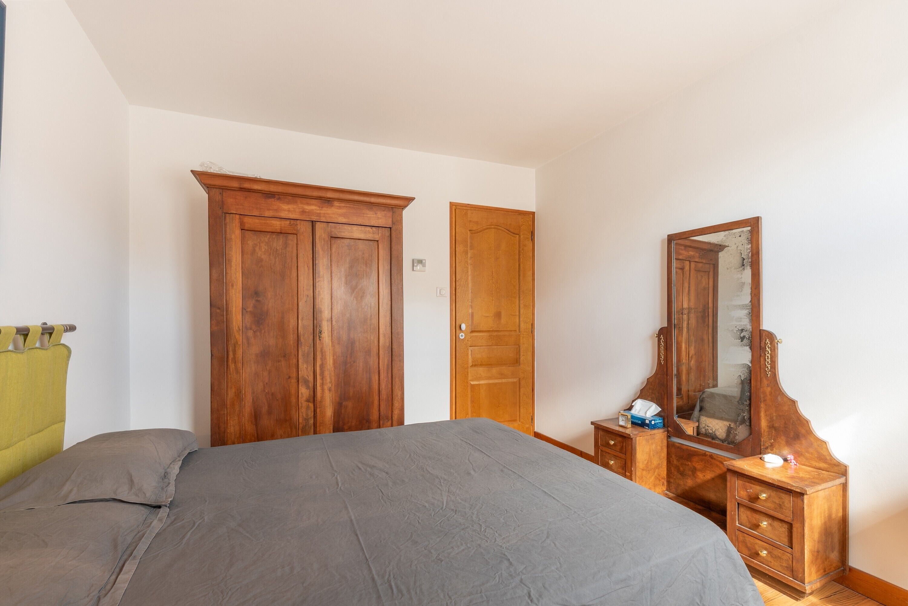 A bedroom with a bed, a wooden wardrobe, a dresser, and a mirror.
