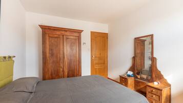 A bedroom with a bed, a wooden wardrobe, a dresser, and a mirror.