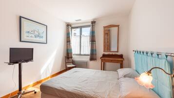 A bedroom with a bed, a TV on a stand, a window with curtains, a mirror, and a lamp.