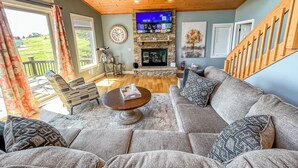Un salon spacieux avec une cheminée en pierre, un grand téléviseur à écran plat et un plafond en bois.
