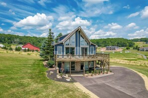 A modern two-story house with a large deck, a stone foundation, and a well-maintained lawn.