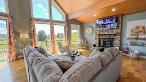 Un salon spacieux avec un grand canapé, une cheminée, un téléviseur et un balcon offrant une vue sur l’extérieur.