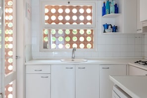 Una cocina con encimera blanca, un lavamanos y una ventana con vidrios redondos.