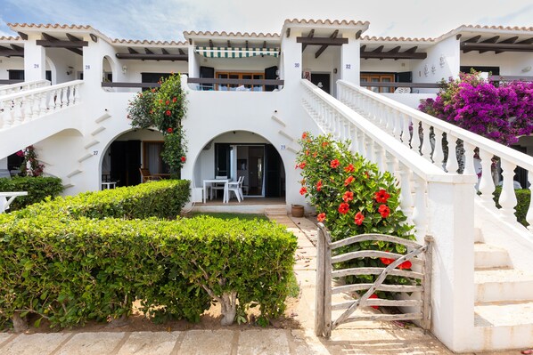 Un bâtiment blanc doté de nombreux balcons, d’un escalier central et d’un jardin bien entretenu.