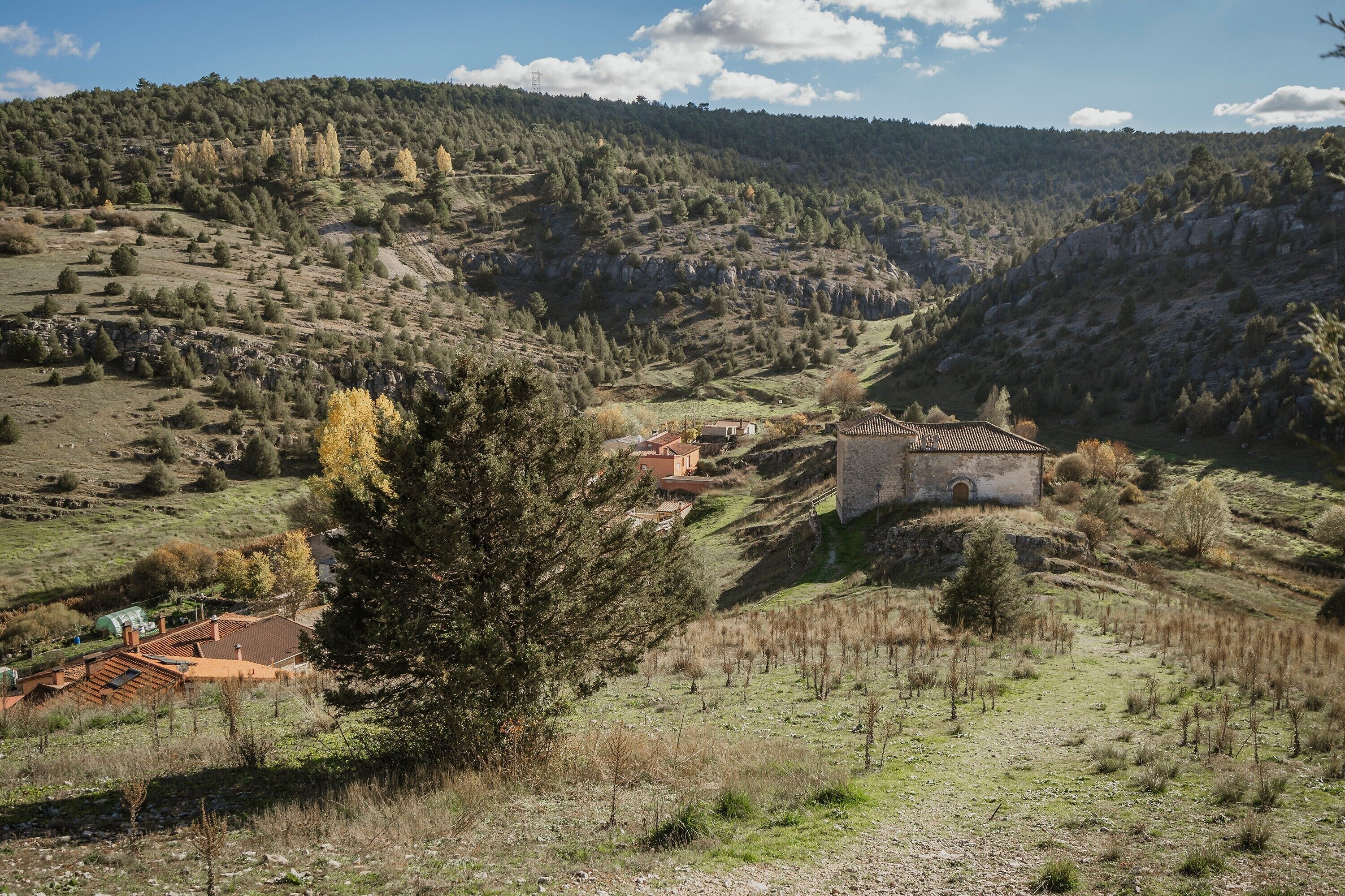 Un paisaje rural con un edificio de piedra y una casa con techo rojo.
