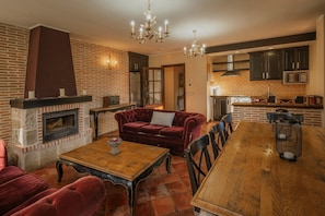 A kitchen with a brick wall, a fireplace, a dining table, and a red sofa.