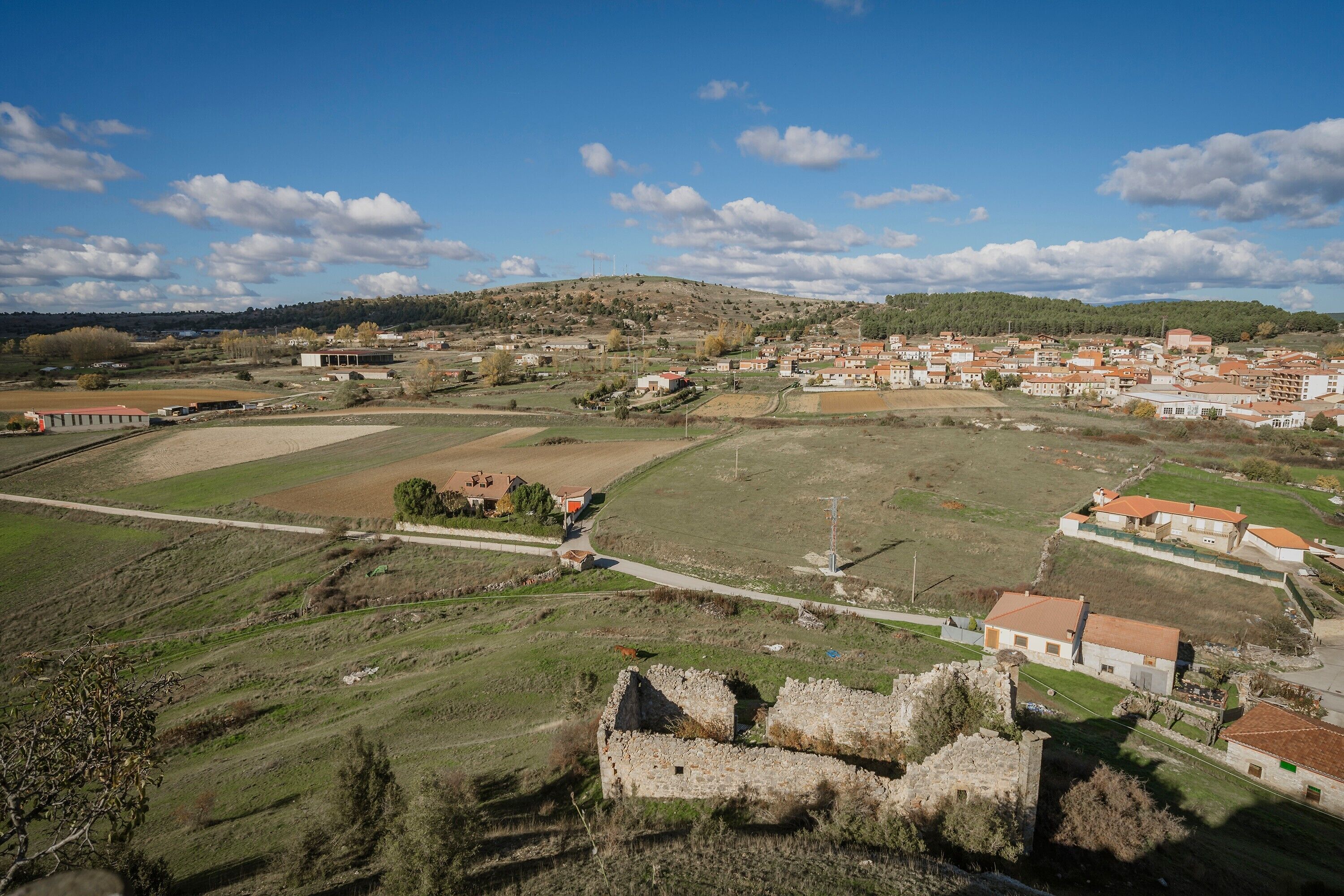 Paisaje rural con un edificio histórico de piedra, campos abiertos y casas dispersas.