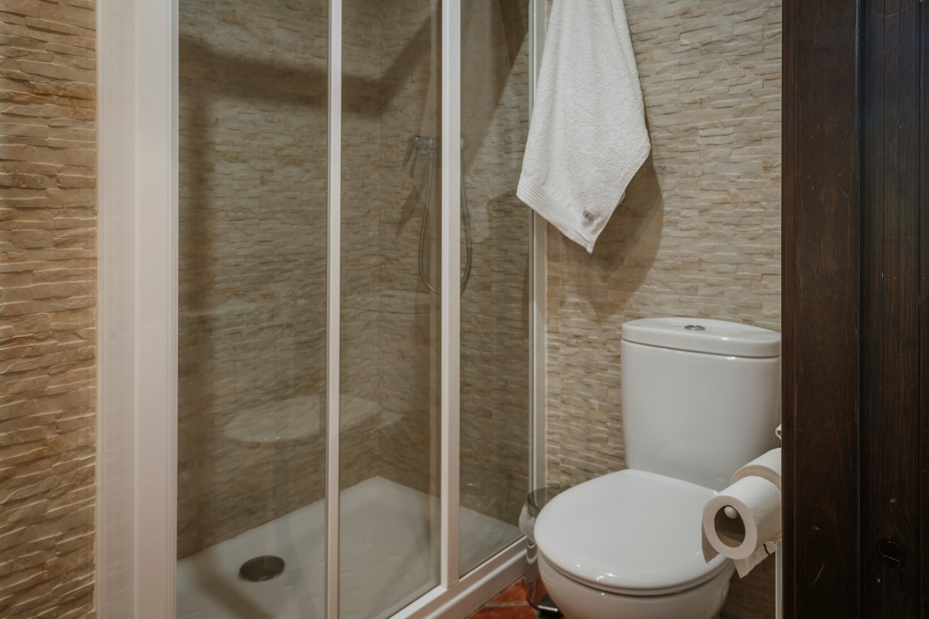 Een badkamer met een douche, toilet en een handdoek aan de muur.