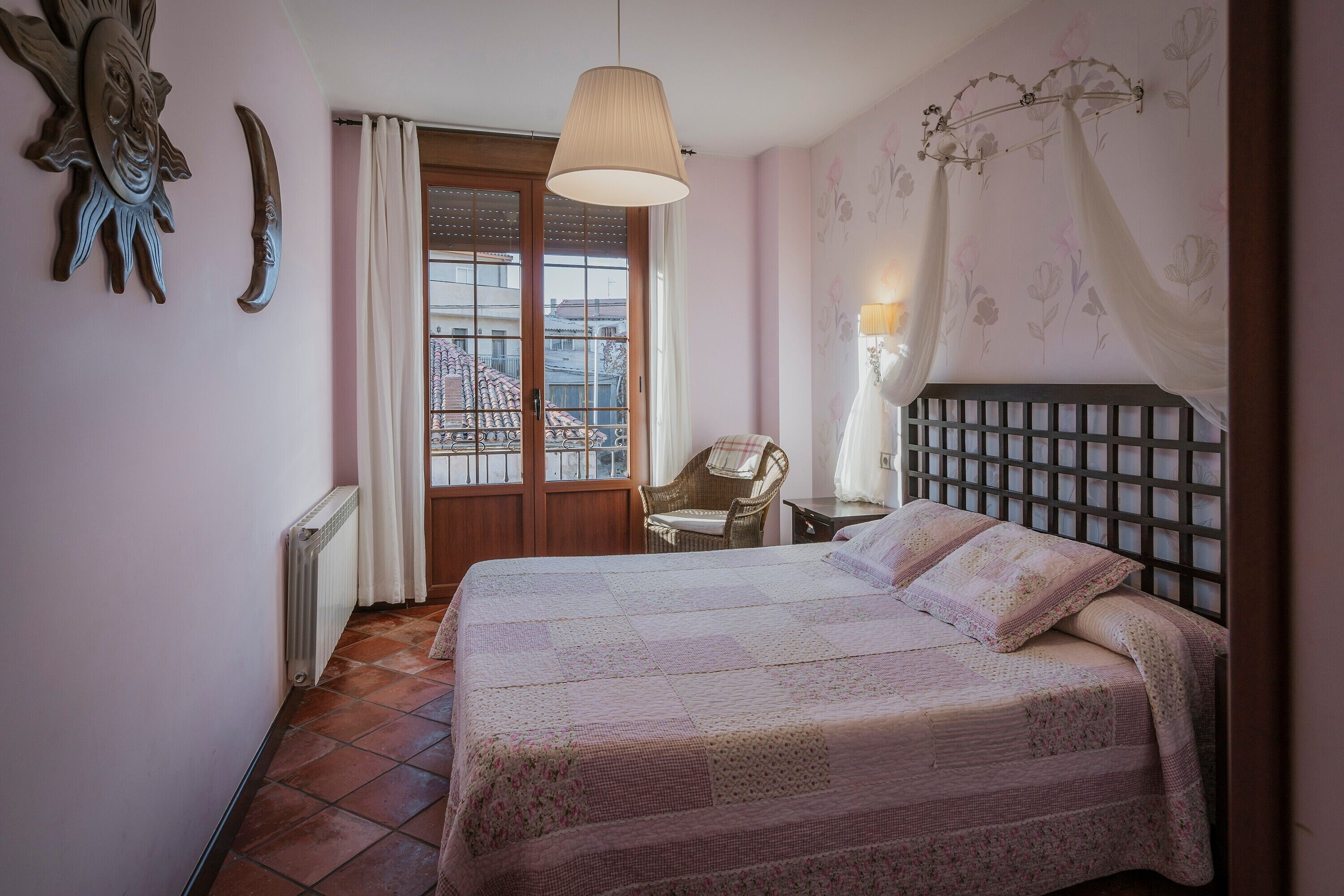 Une chambre à coucher comprenant un lit, une chaise, une fenêtre avec des rideaux, un radiateur et un élément décoratif mural.