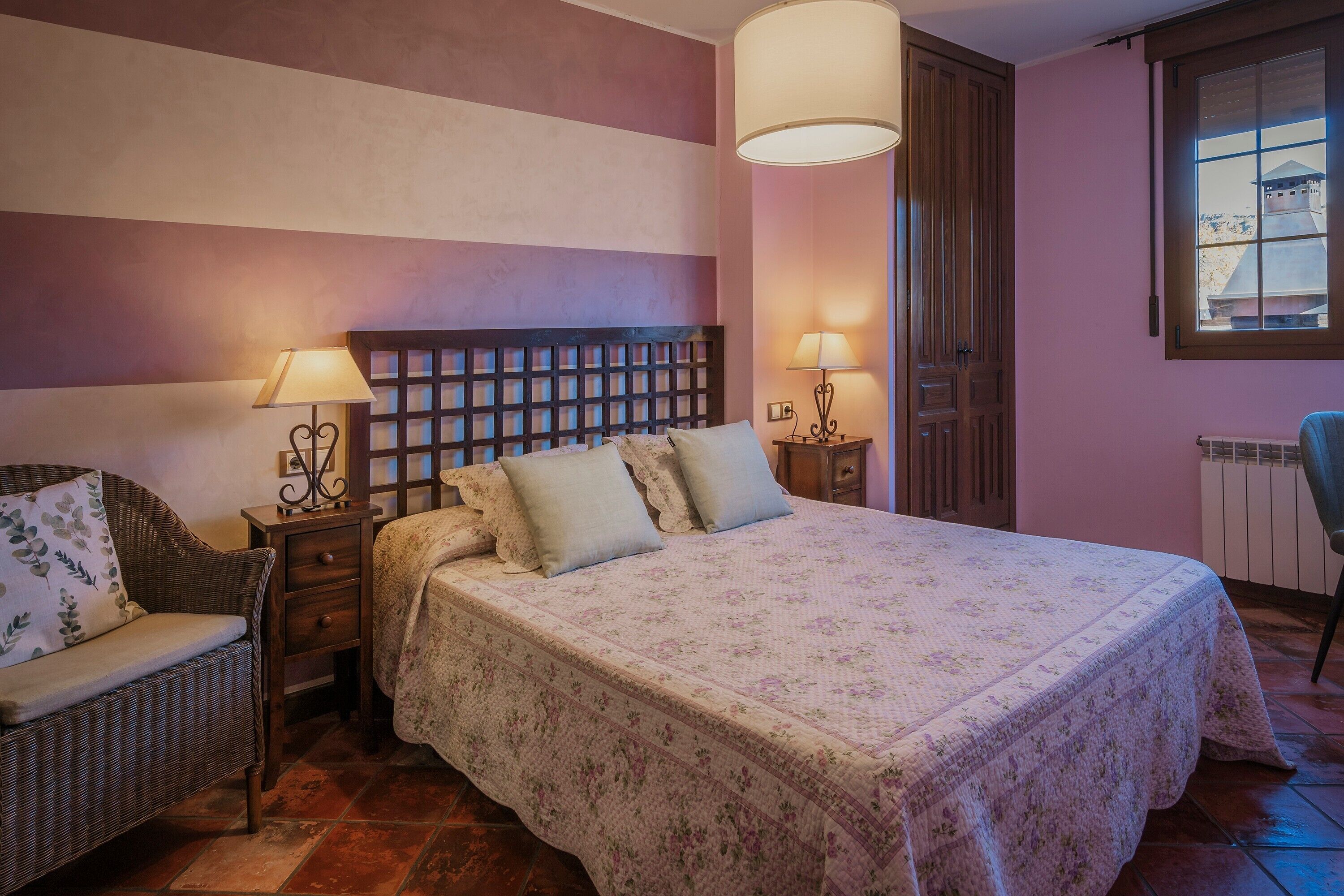 A bedroom with a bed, two bedside tables with lamps, a chair, a window, and a radiator.