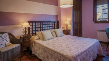 A bedroom with a bed, two bedside tables with lamps, a chair, a window, and a radiator.