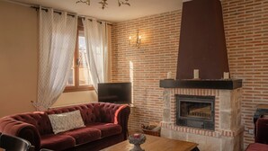 A living room with a brick fireplace, a red sofa, a wooden table, and a television. - Apartment 'Entrada Rio Lobos Grande' with Mountain View, Private Terrace and Wi-Fi (Hontoria Del Pinar)