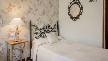 Une chambre à coucher avec un lit, une table de chevet avec une lampe, un miroir fixé au mur et un papier peint à motifs floraux.