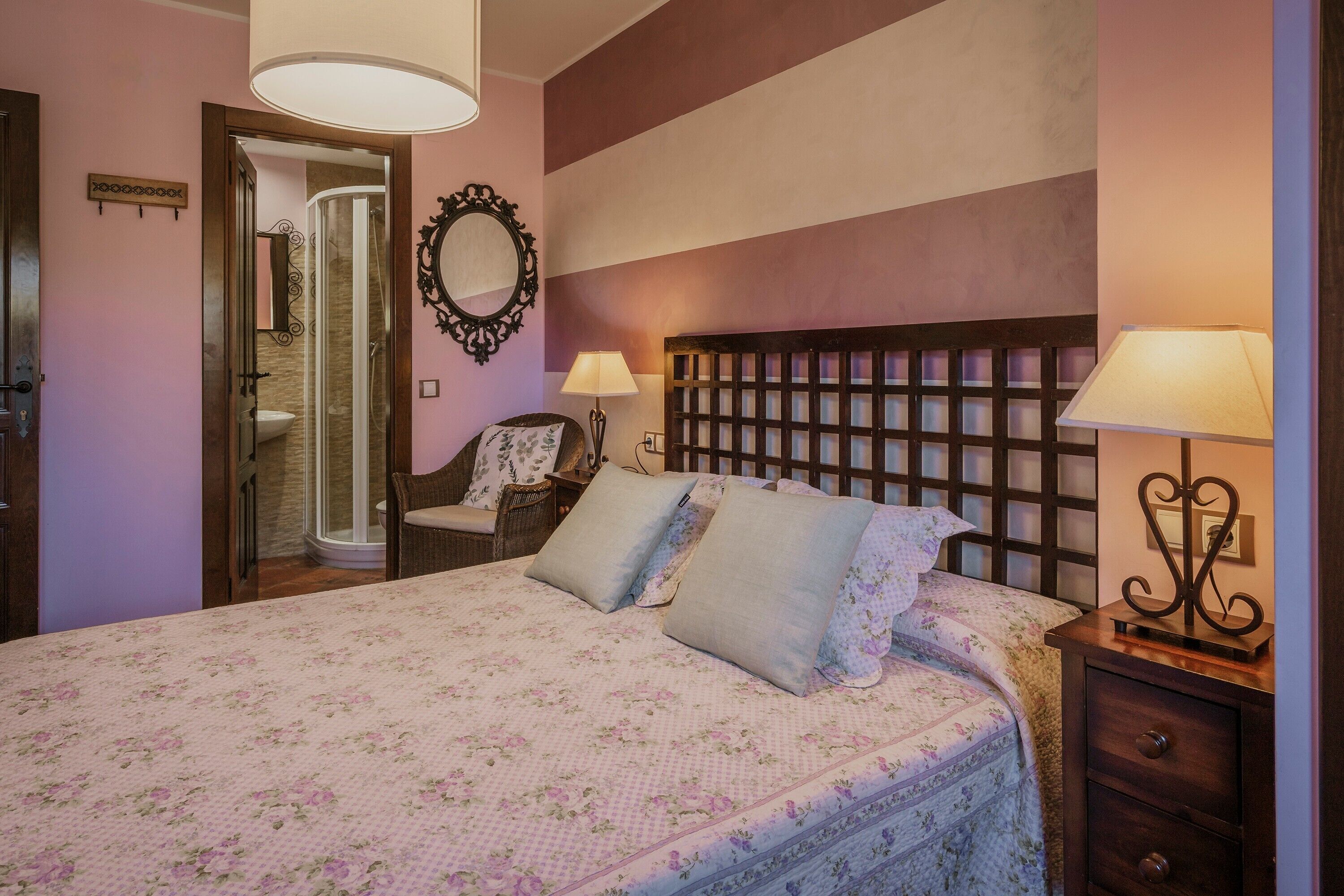 Ein Schlafzimmer mit einem Bett, zwei Nachttischlampen, einem Nachttisch, einem Sessel, einem Spiegel und einer zur Toilette führenden Tür.