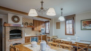A kitchen with a brick fireplace, wooden cabinets, a dining table with chairs, and pendant lighting. - Country House 'Entrada Rio Lobos I' with Mountain Views, Private Terrace and Wi-Fi (Hontoria Del Pinar)