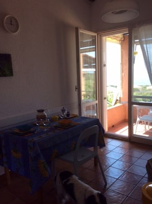 A dining area with a table set for two, a dog, and a sliding glass door leading to an outdoor patio. - Apartment 'La Terrazza Sulla Baia Di Calvi' with Sea View, Private Terrace and Private Garden (Lumio)