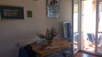 Un coin repas avec une table en bois, des chaises, une horloge, une affiche et une porte-fenêtre coulissante donnant sur un espace extérieur.