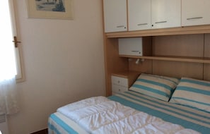 A bedroom with a bed, a nightstand, a dresser, and a shelf with a picture frame. - Apartment 'La Terrazza Sulla Baia Di Calvi' with Sea View, Private Terrace and Private Garden (Lumio)