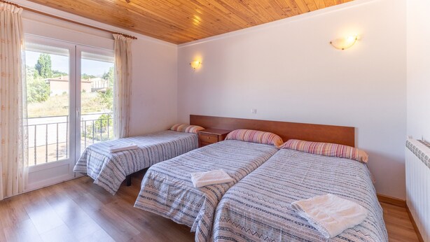 Una habitación con dos camas, techo de madera, balcón con cortinas y vistas al exterior.