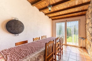 Un comedor con una mesa, sillas, una lámpara colgante y vistas a través de una puerta de vidrio.