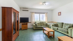 Una sala de estar con un sofá, televisión, mueble y una ventana con cortinas.