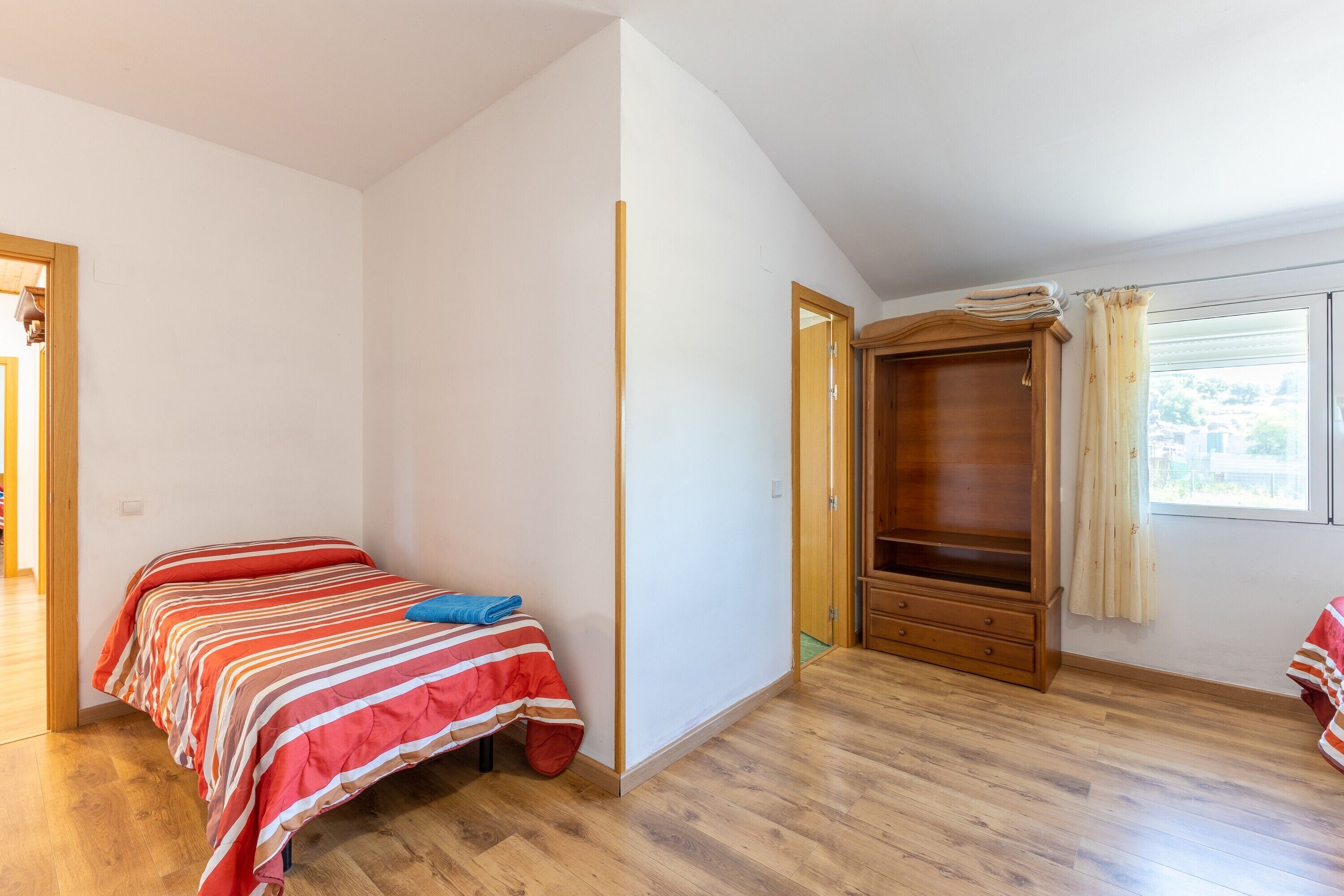 Ein Schlafzimmer mit einem Bett, einem Holzschrank und einem Fenster mit Vorhängen.