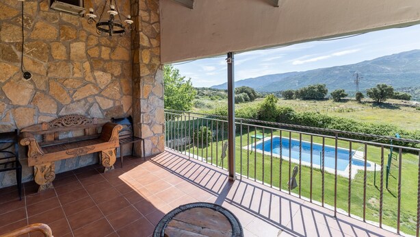 Un muro de piedra, un banco de madera y vistas a una piscina desde un balcón.