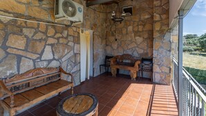 Un patio con paredes de piedra, un banco de madera, una mesa redonda pequeña y un ventilador de techo.