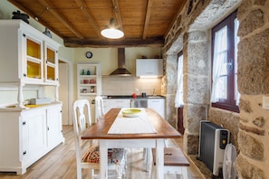 Una cocina rústica con una mesa de madera, armarios blancos, paredes de piedra y una chimenea de piedra.