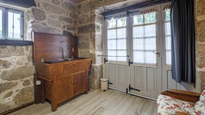 Una habitación con paredes de piedra, un armario de madera, una ventana con cortinas y una puerta.