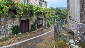 Un edificio de piedra con una puerta roja, un sendero estrecho y un muro de piedra con una puerta de madera.