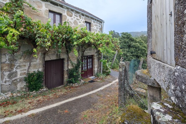 Un edificio de piedra con una puerta roja, un sendero estrecho y un muro de piedra con una puerta de madera.
