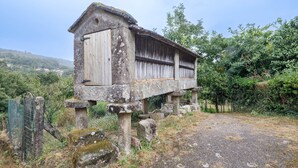 Una estructura rústica de piedra con puerta y ventana de madera, sostenida por pilares de piedra, rodeada de follaje.