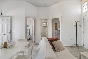 A white-walled room with a sofa, a dining table, and a coat rack.
